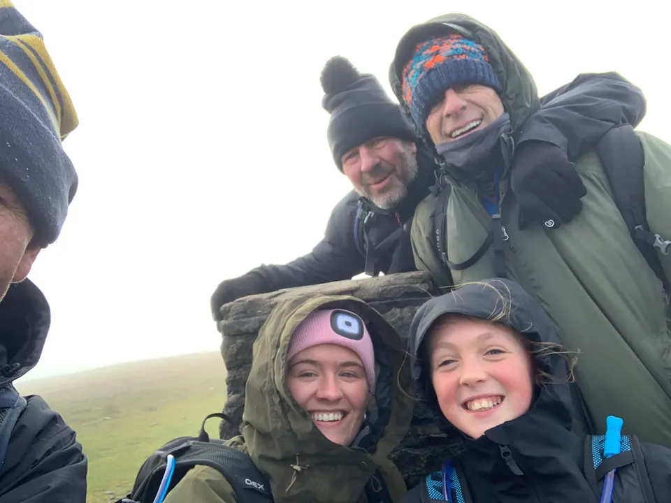 Walkers in waterproof clothing smile for a group photograph on the hills.