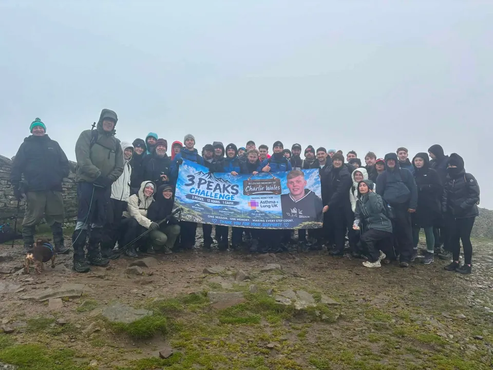 The walking group gathers on a misty hillside with a Three Peaks Challenge fundraising banner.