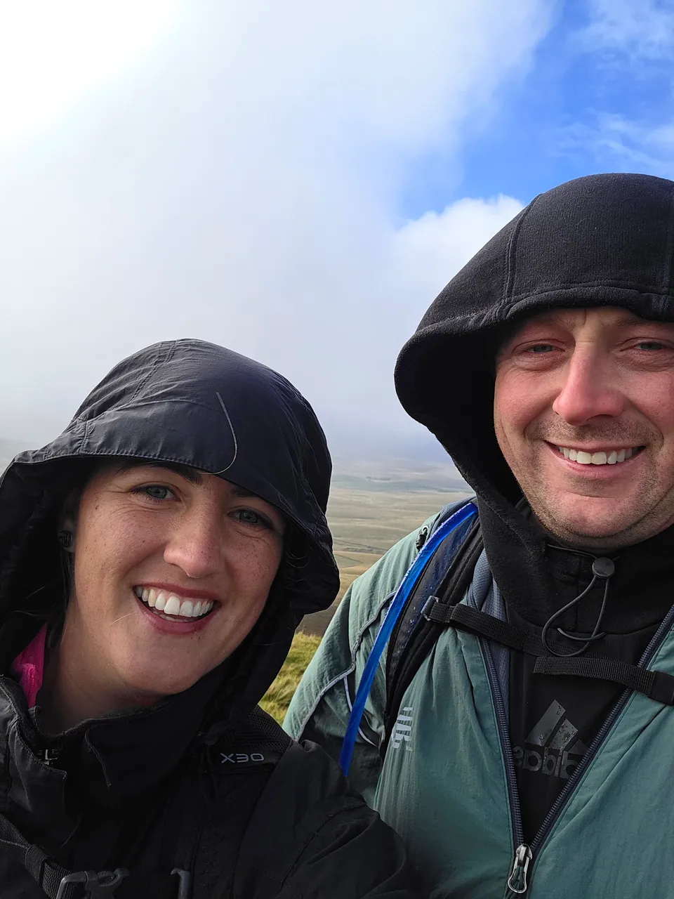 Two walkers in waterproof jackets take a photograph on the hills.
